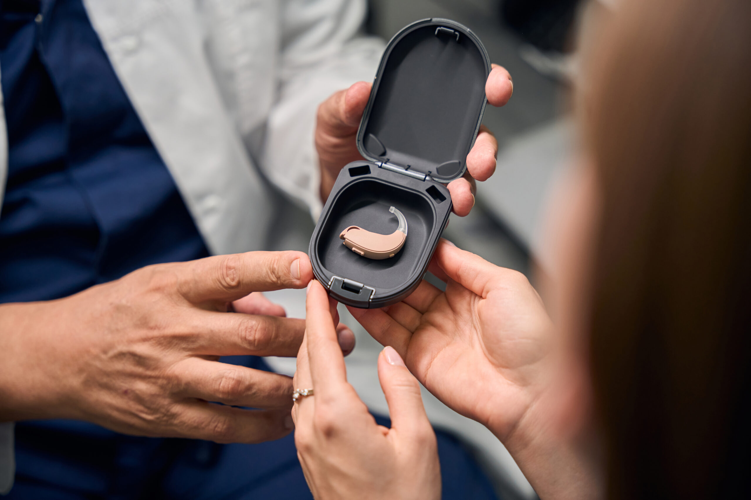 Patient reaching towards the hearing aid in a case Hörgeräte mit Rauschunterdrückungstechnologie erleben