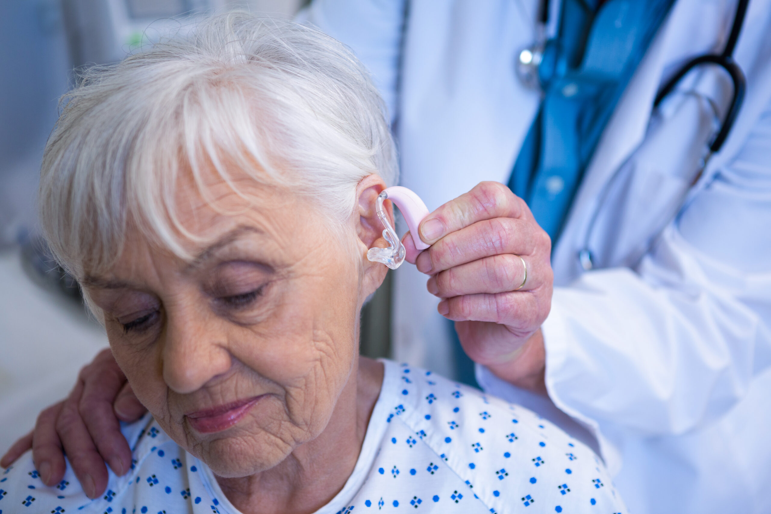 Doctor inserting hearing aid in senior patient ear Tragekomfort im Alltag von Hörgeräten erhöhen